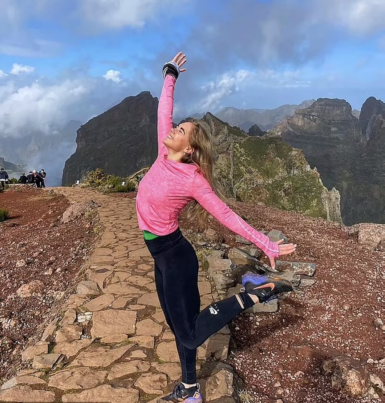 smiling girl in pink top and black tights poses on a cobbled mountain walkway